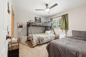 Une chambre avec un lit superposé, un ventilateur de plafond, une fenêtre avec des rideaux et une petite table de chevet sur laquelle se trouve une boîte de mouchoirs.
