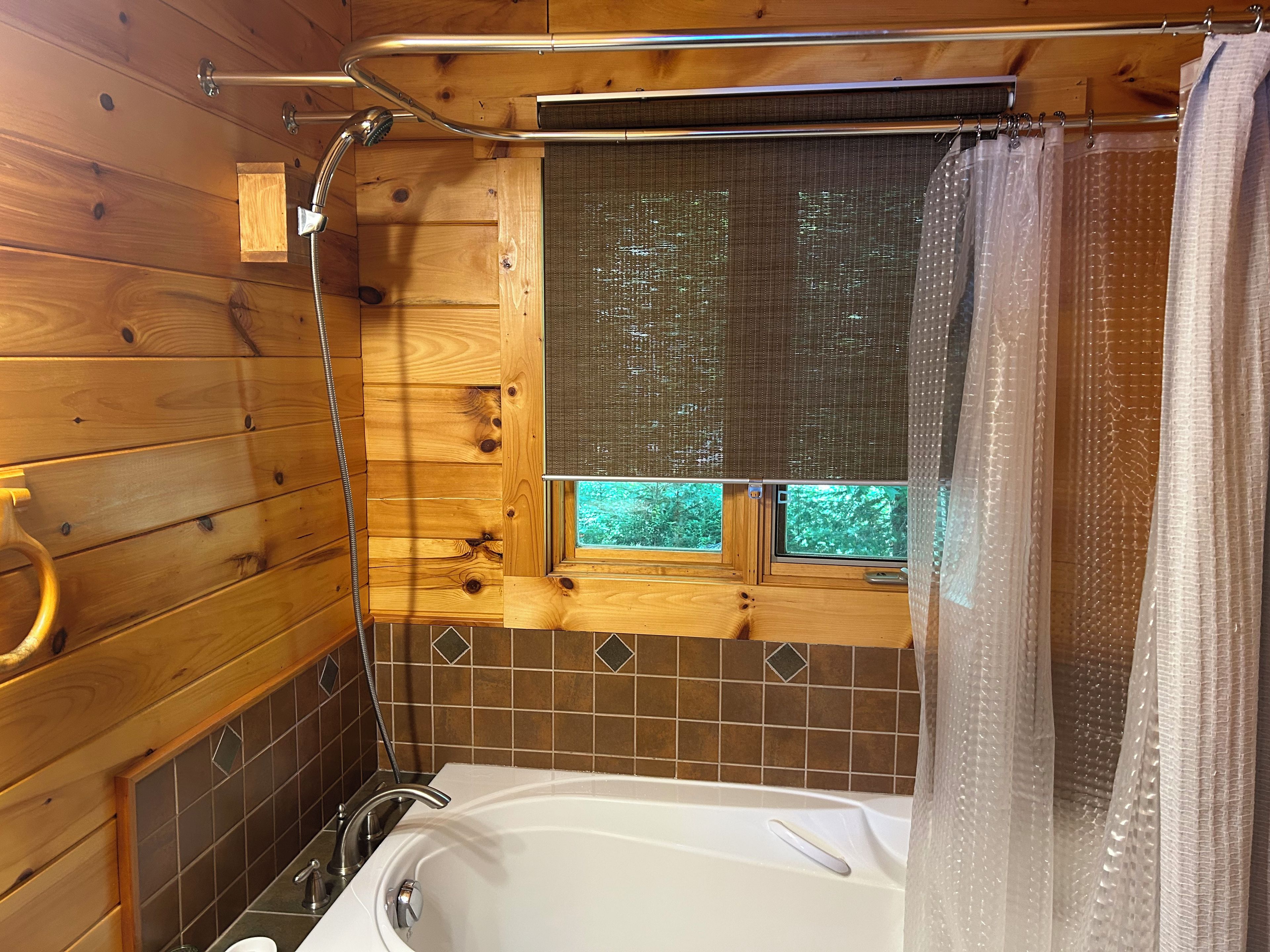 A wooden cabin bathroom with a bathtub, shower, and window with a view.