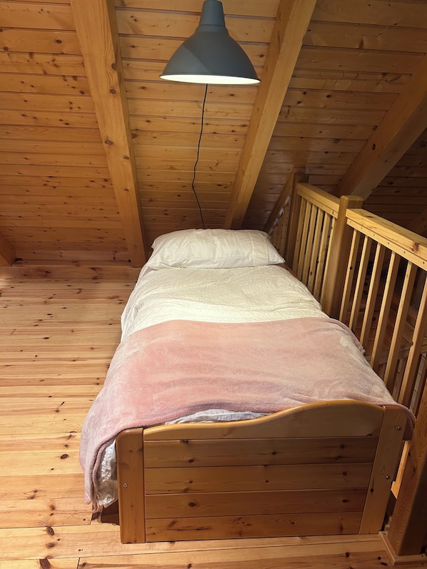 A single wooden bed with a white and pink blanket, a wooden headboard, and a hanging lamp.