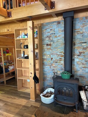 A rustic interior with a wooden loft, a stone wall, and a wood-burning stove.