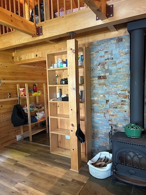 A cozy room with a wooden bookshelf, a brick wall, and a wood-burning stove.