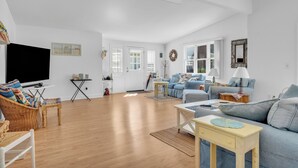 A spacious living room with a large flat-screen TV, a blue sofa set, a wooden coffee table, and a wicker chair. - Saybrook Point Pool House (Old Saybrook)