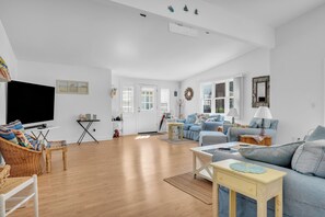 A spacious living room with a large flat-screen TV, a blue sofa set, a wooden coffee table, and a wicker chair. - Saybrook Point Pool House (Old Saybrook)