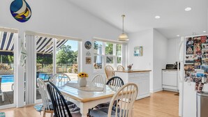A bright kitchen with white cabinets, a dining table with chairs, and a view of a pool through the glass door. - Saybrook Point Pool House (Old Saybrook)