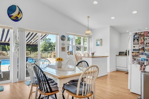A bright kitchen with white cabinets, a dining table with chairs, and a view of a pool through the glass door. - Saybrook Point Pool House (Old Saybrook)