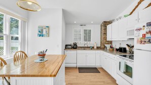A modern kitchen with white cabinetry, a wooden dining table, and a hanging light fixture. - Saybrook Point Pool House (Old Saybrook)