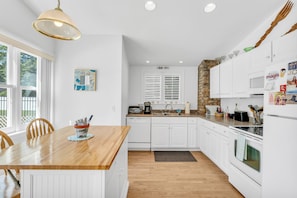 A modern kitchen with white cabinetry, a wooden dining table, and a hanging light fixture. - Saybrook Point Pool House (Old Saybrook)