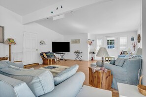 A spacious living room with a large sofa, a television, and a dining area with a table and chairs.