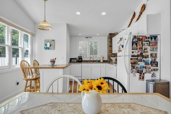 A modern kitchen with white cabinetry, a dining table with chairs, a hanging light fixture, and a refrigerator covered in photos.