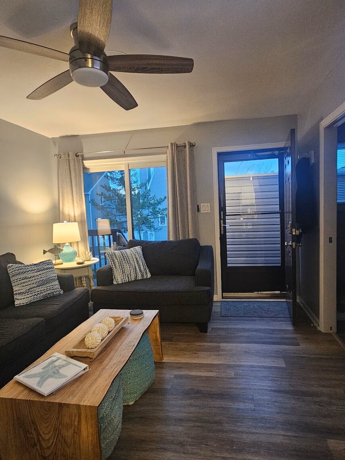 A living room with a ceiling fan, a sofa, a coffee table, and a view through a door to the outside.