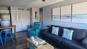 A modern living room with a ceiling fan, a sofa, a coffee table, and a view of the ocean. - Coastal Comfort - 2BR/2BA Condo in North OCMD - Walk to Beach, Dining & Fun (Ocean City)