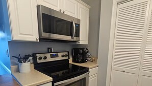 A kitchen with white cabinets, a stainless steel microwave, a coffee maker, and an oven. - Coastal Comfort - 2BR/2BA Condo in North OCMD - Walk to Beach, Dining & Fun (Ocean City)