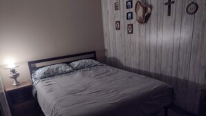 Un letto con testiera, un comodino con una lampada, e una parete con quadri e un cappello.