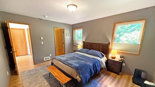 A bedroom with a bed, bedside table, lamp, and a window with a view. - Riverfront A-Frame with Hot Tub, Game Room and Fire Pit - Sleeps 10, Dogs OK (Granite Falls)