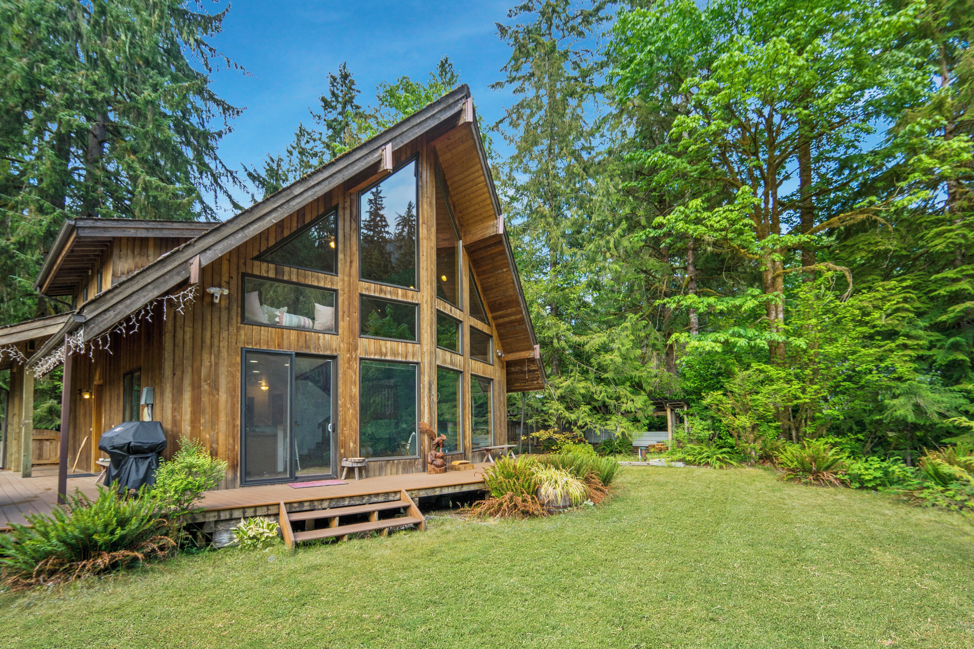 A modern wooden cabin with large windows, a deck, and a forested backdrop.