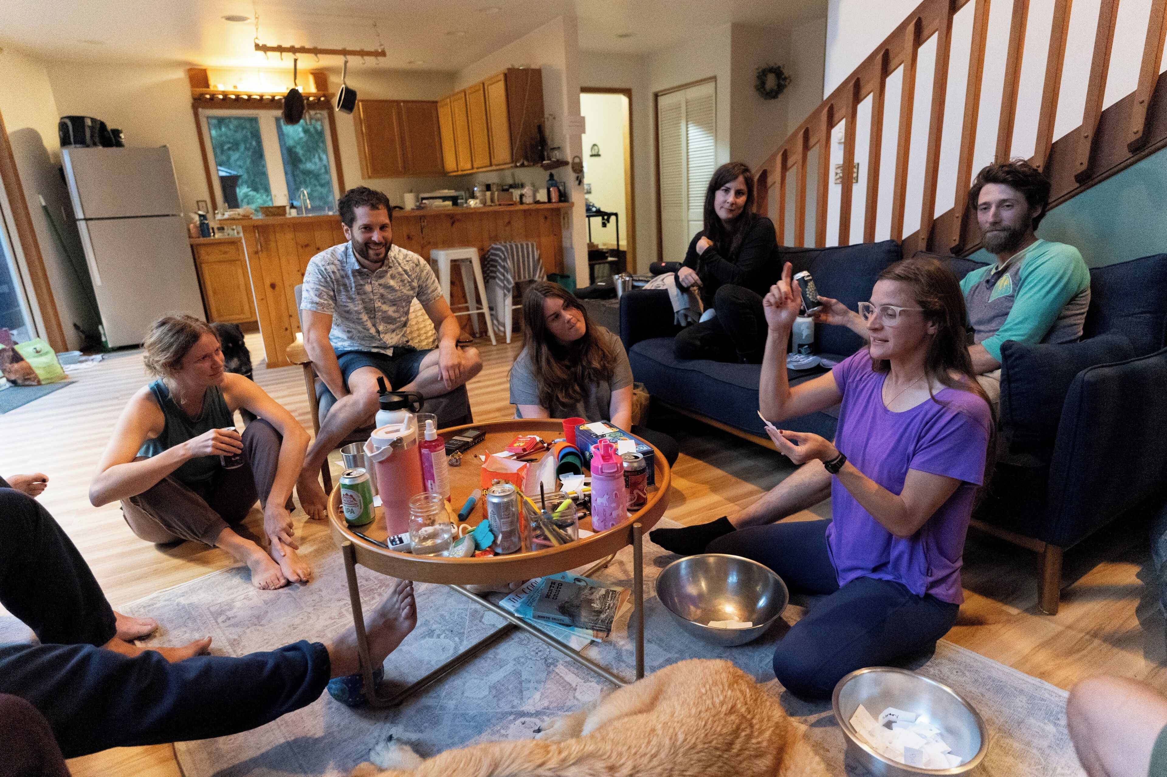 Un groupe de personnes est assis sur le sol dans un salon, avec une cuisine en arrière-plan.
