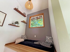 A cozy room with a bed, a window with a view of greenery, a hanging light fixture, and wall-mounted shelves. - Riverfront A-Frame with Hot Tub, Game Room and Fire Pit - Sleeps 10, Dogs OK (Granite Falls)