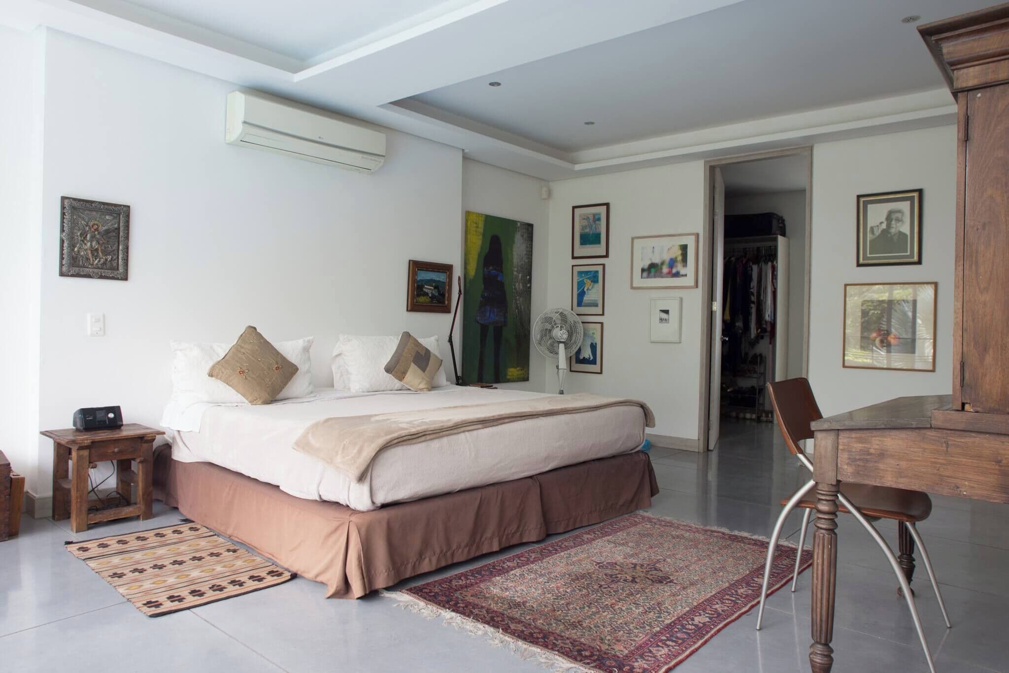 A bedroom with a bed, bedside table, and a fan. There is a door leading to a closet.