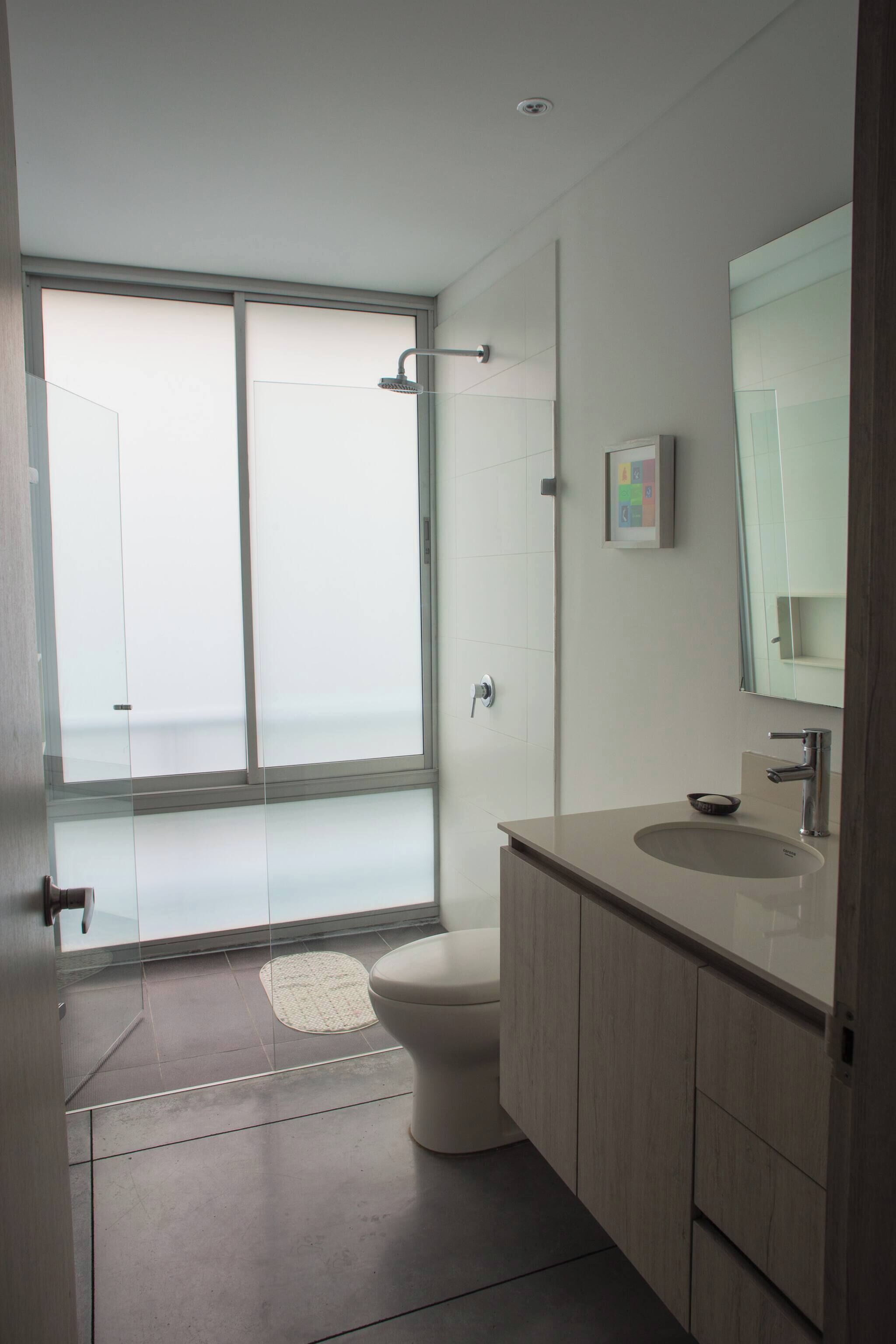 A modern bathroom with a glass shower enclosure, a toilet, a sink with a mirror, and a small rug on the floor.
