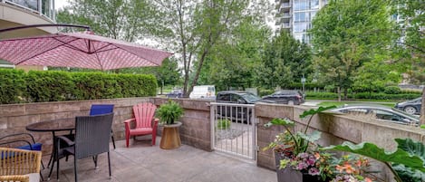 An outdoor patio area with a table, chairs, and a red umbrella.
