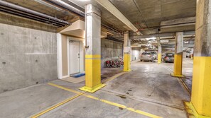 En parkeringskælder med betondæk, gule sikkerhedsmærker og flere parkerede biler.