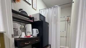Una kitchenette compacta con cafetera, microondas y estantes de almacenamiento.