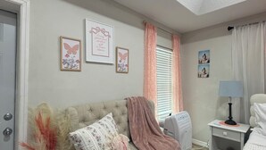 Un dormitorio con cama, una mesita de noche con lámpara, un sofá con almohadones decorativos, un florero con plantas secas y una luz en el techo.