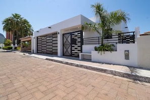 A modern building with a white facade, two black gates, and a paved driveway. - Modern home close to pickleball, beach, pool (La Manga)