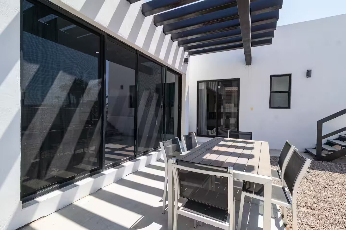 Une terrasse extérieure moderne avec un mur de verre, une table avec des chaises et un escalier menant à un niveau supérieur.