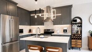 Eine moderne Küche mit einem Edelstahlkühlschrank, einer zentralen Kochinsel mit Barhocker und einem Weinkühlschrank.