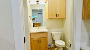 A bathroom with a toilet, sink, and wooden cabinets. - Tiny Guest House close to Lake Elmdale and all NWA has to offer! (Springdale)