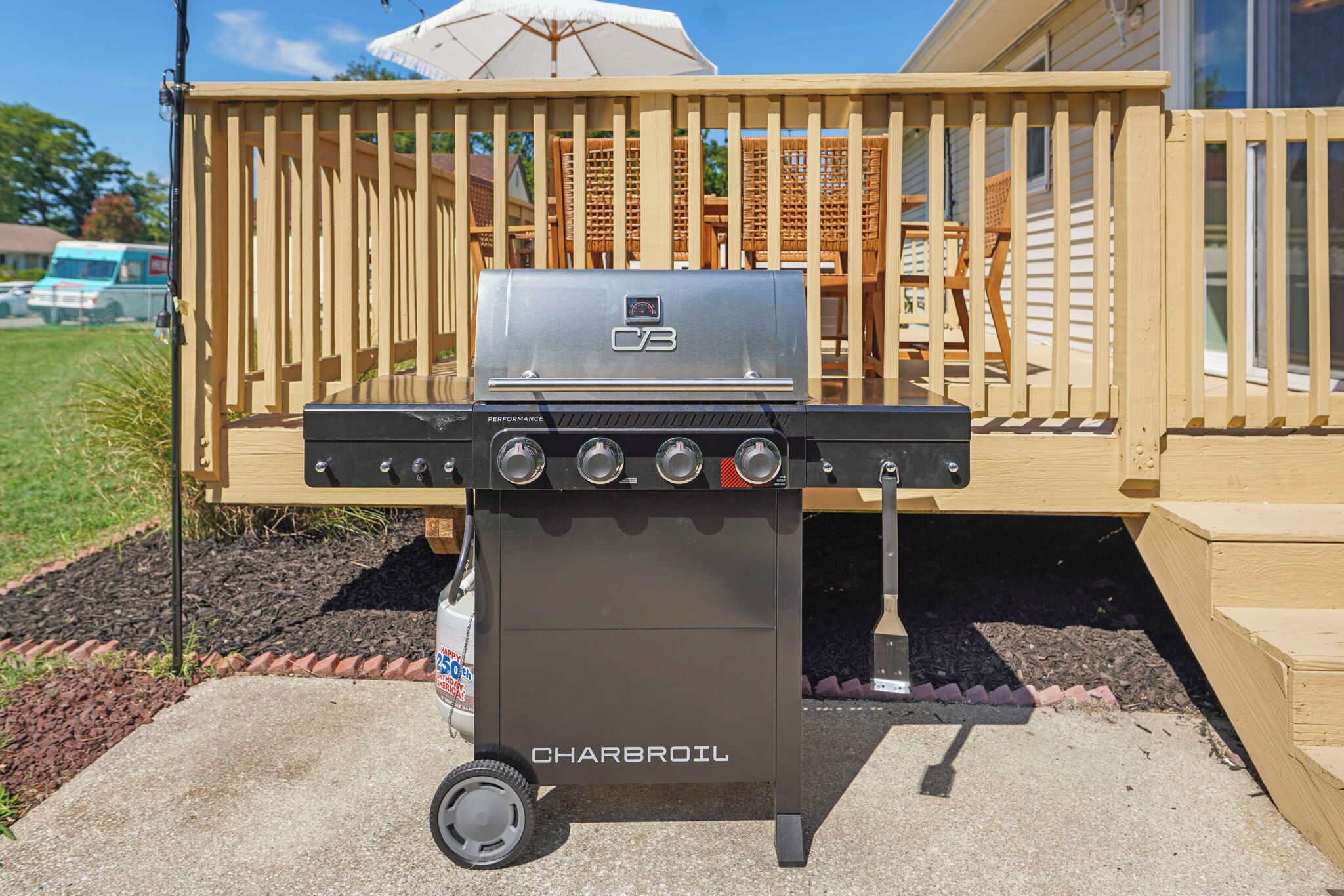 A charcoal grill with a digital display, labeled 'Charbroil,' positioned on a concrete patio with a wooden deck and outdoor furniture in the background.