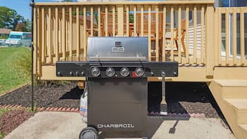 A charcoal grill with a digital display, labeled 'Charbroil,' positioned on a concrete patio with a wooden deck and outdoor furniture in the background.