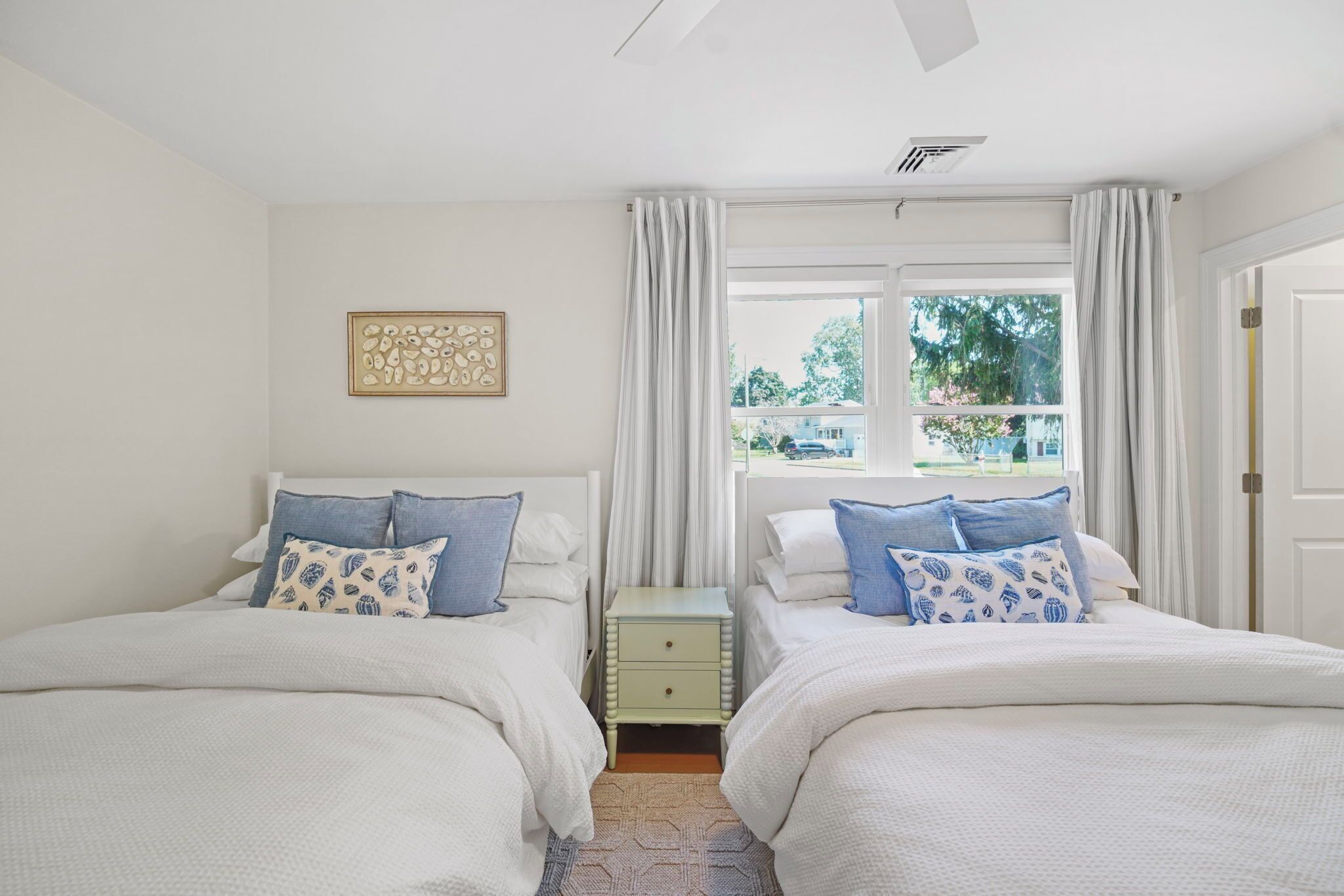 A bedroom with two beds, a nightstand, a window with curtains, and a ceiling fan.