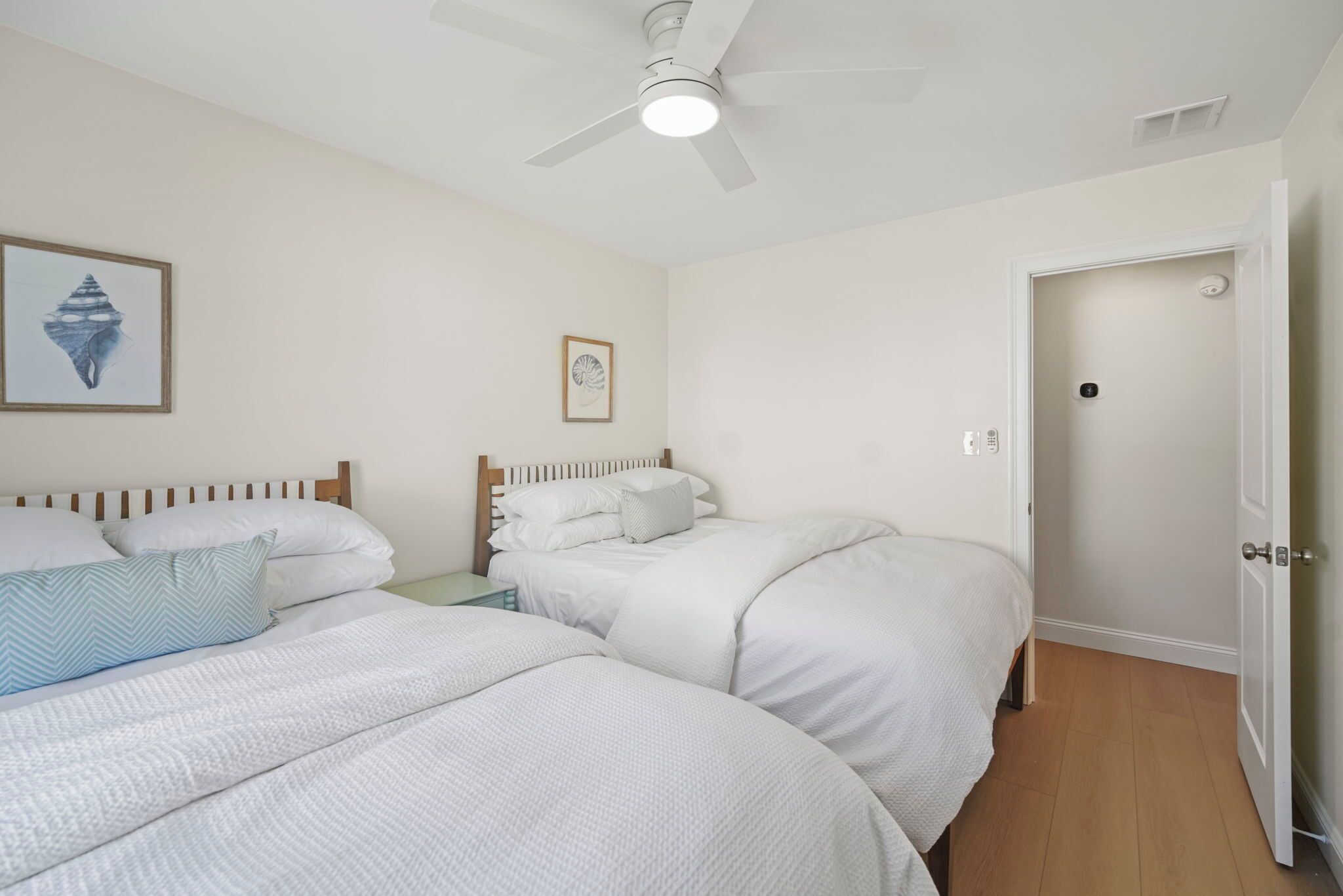 A bedroom with two beds, a ceiling fan, and a door.