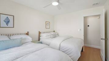 A bedroom with two beds, a ceiling fan, and a door.