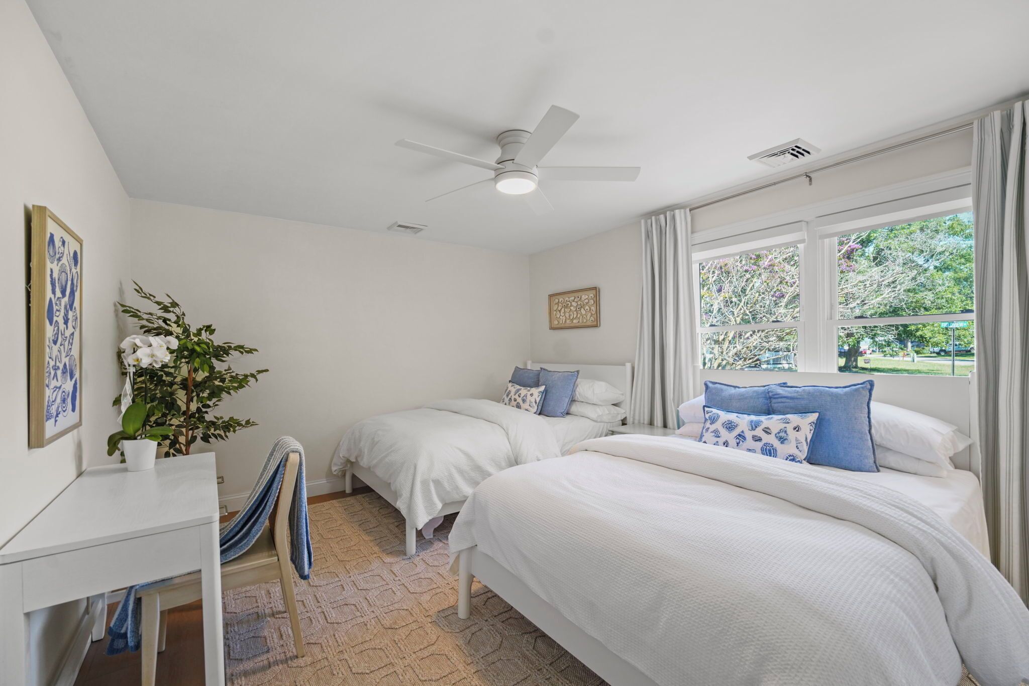 A bedroom with two beds, a ceiling fan, a window with curtains, a desk, and a chair.