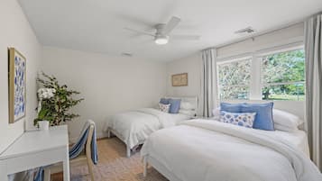 A bedroom with two beds, a ceiling fan, a window with curtains, a desk, and a chair.