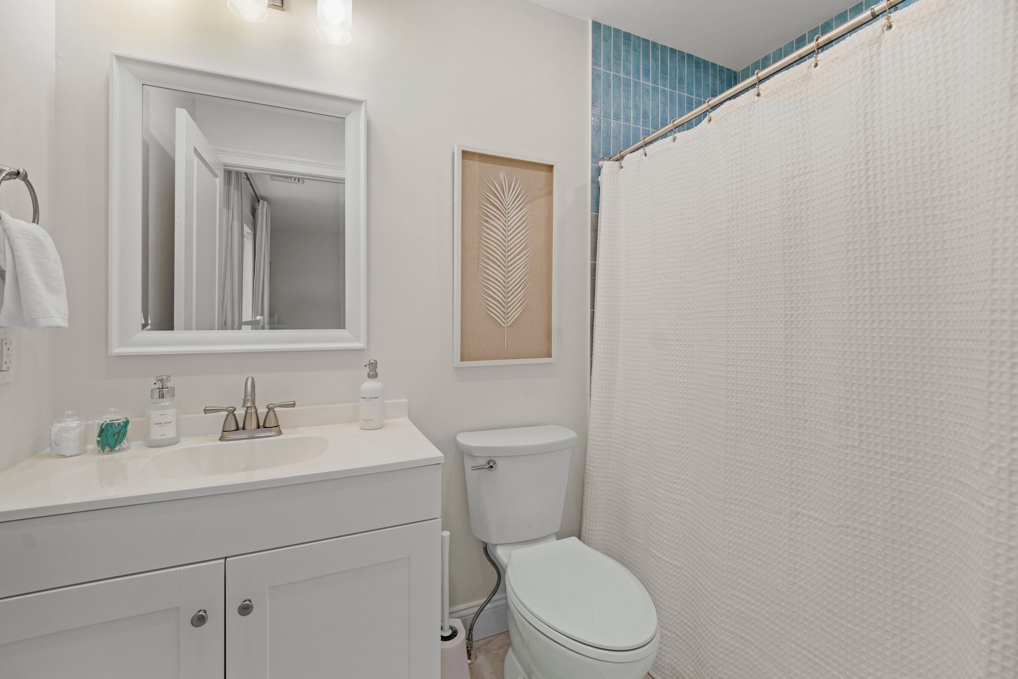 Een badkamer met een wit wastafel, een spiegel, een toilet en een douchegordijn.