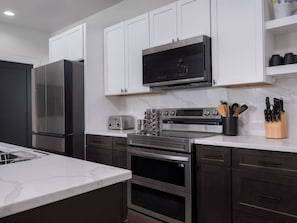 A modern kitchen with stainless steel appliances, white cabinets, and a marble countertop. - Stone Peak Mountain Retreat - New w/ ac (Driggs)