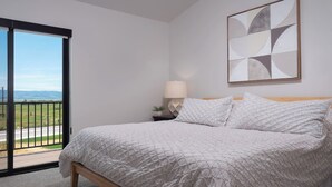 Et soveværelse med en seng, et natbord, en lampe og udsigt gennem en skydedør.