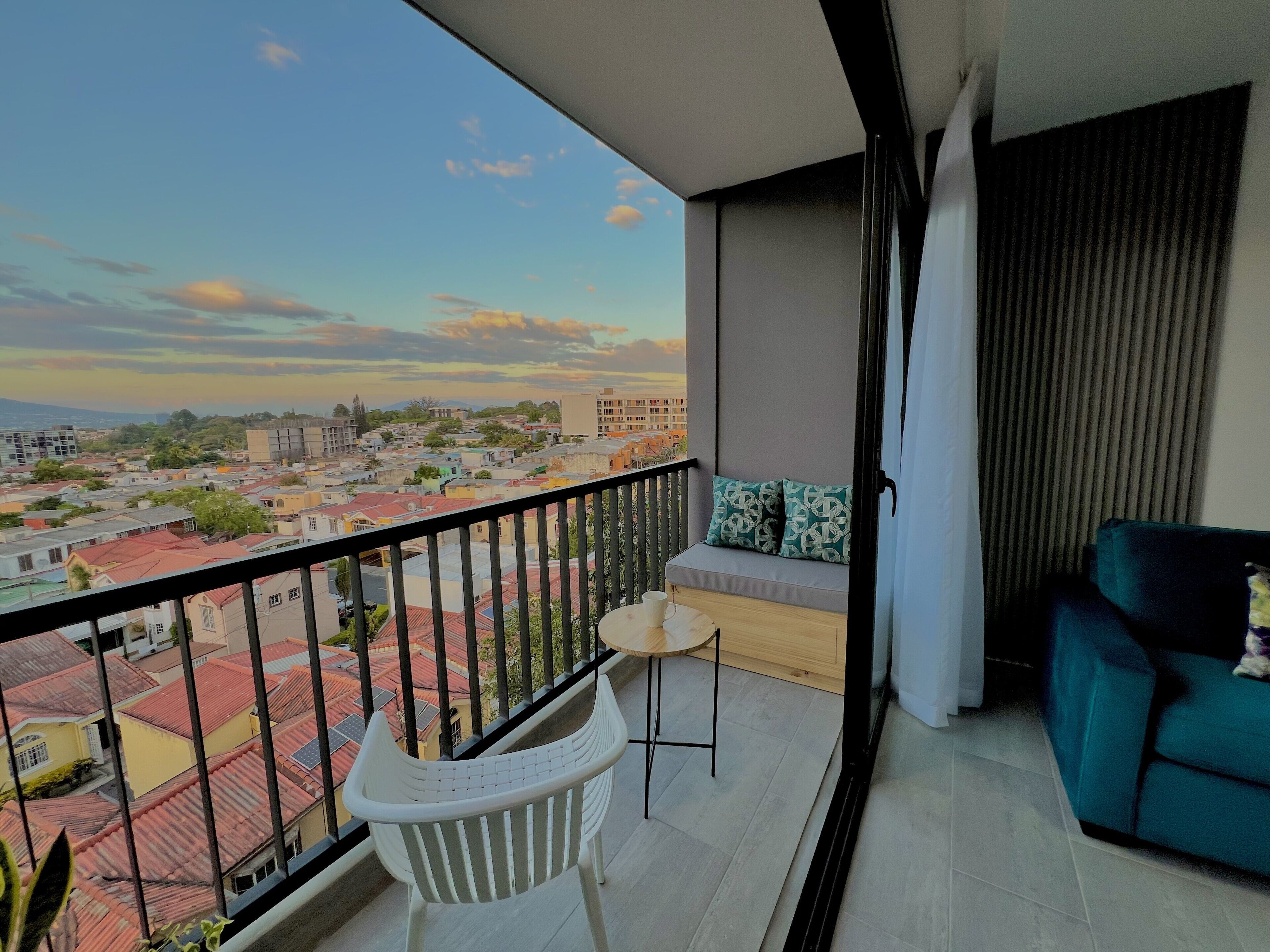 A balcony with a view of a cityscape, a white chair, a small table, and a blue sofa.
