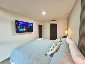 Ett hotellrum med en säng, en väggmonterad tv, en luftkonditioneringsanläggning och en dörr.
