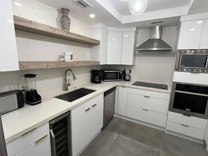Una cocina moderna con muebles blancos, microondas integrado, cafetera y tostadora.