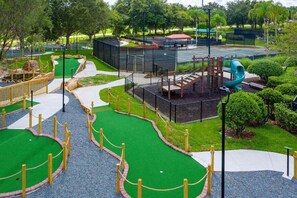 Ein Minigolfplatz mit einem grünen Putting-Bereich, einem Spielbereich mit Rutsche und einem umzäunten Weg.