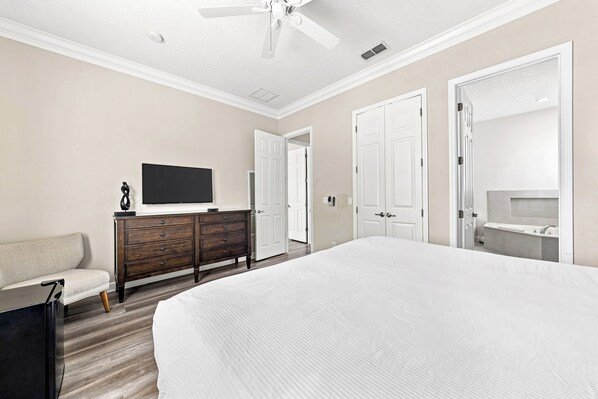 A hotel room with a large bed, a TV on a dresser, a sofa, and a ceiling fan. - Beautiful Home with Private Pool and Balcony, Near Attractions (Kissimmee)