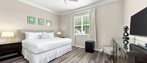 A bedroom with a bed, bedside tables, a ceiling fan, a window with curtains, and a television on a dresser.