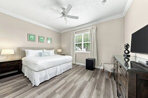 Ein Schlafzimmer mit einem Bett, Nachttischen, einem Deckenventilator, einem Fenster mit Vorhängen und einem Fernseher auf einer Kommode.