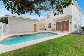 Ein zweistöckiges Haus mit Swimmingpool, eingezäunter Garten und einem Baum, der Schatten spendet.