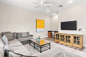 A living room with a sectional sofa, a coffee table, a TV, and a wooden cabinet. - Beautiful Home with Private Pool and Balcony, Near Attractions (Kissimmee)